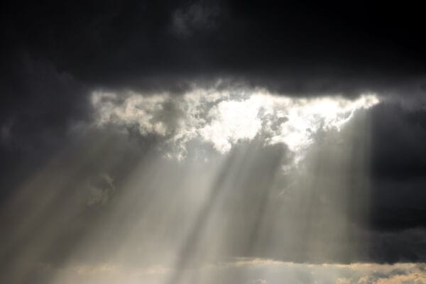 Light sun beams shine down through a break in dark grey clouds.