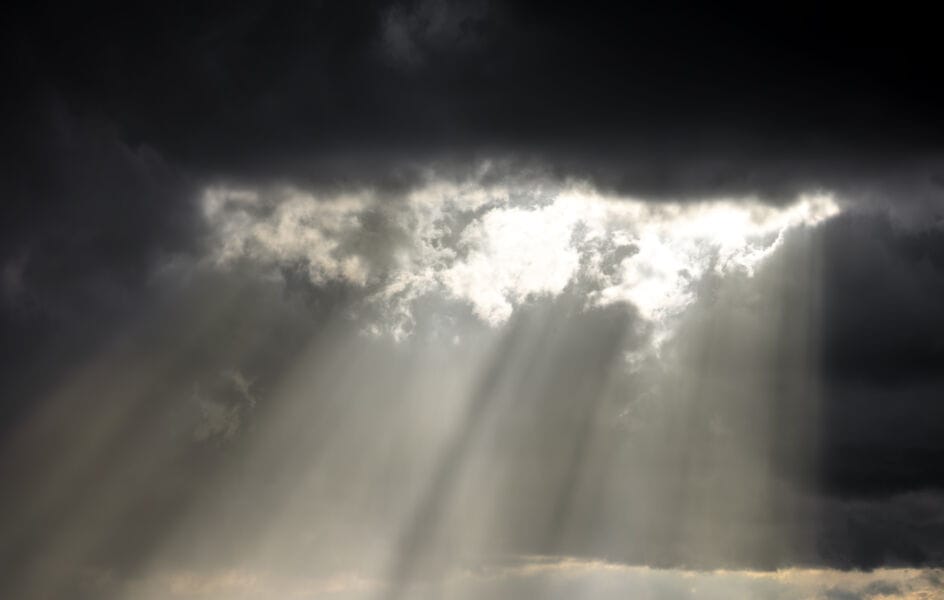 Light sun beams shine down through a break in dark grey clouds.
