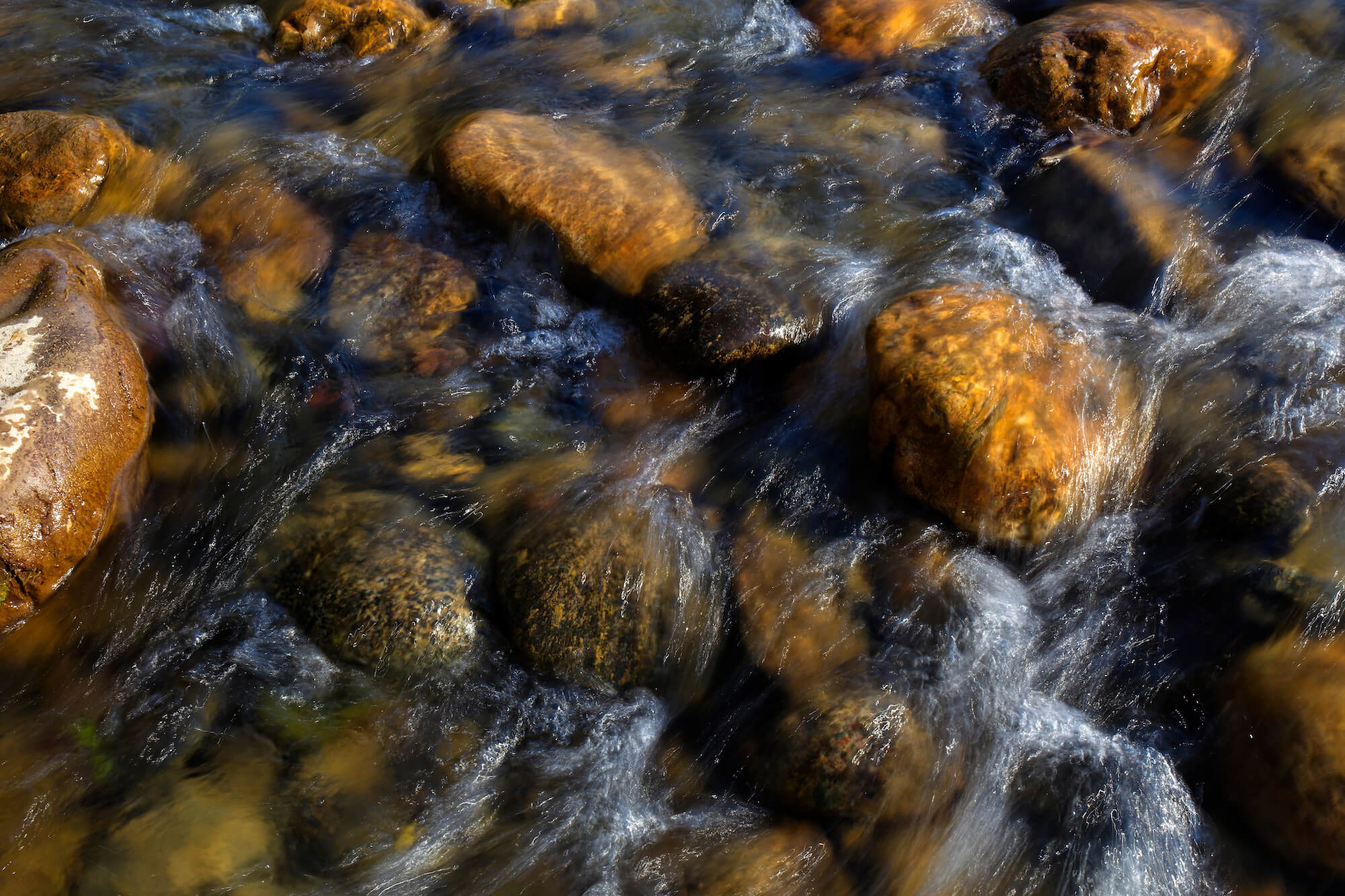 Looking down into a creek at brown and gray rocks under flowing water.