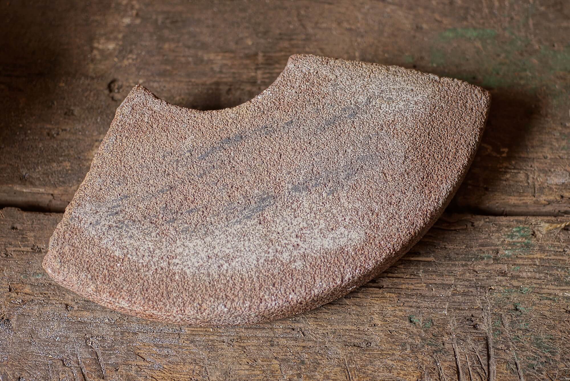 close view of a light reddish, curved dry whetstone resting on a wood workbench